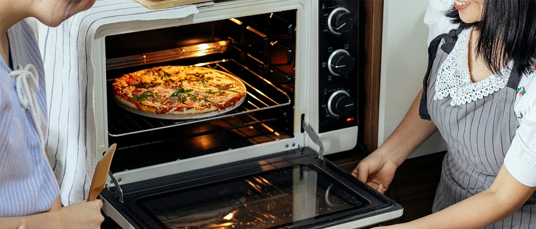Twee mensen die een pizza uit de oven halen.