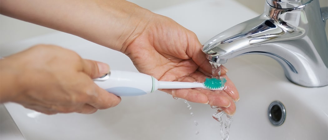 Een elektrische tandenborstel die boven de lavabo wordt uitgespoeld
