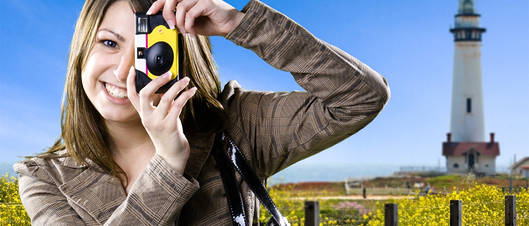 Een vrouw die een foto trket met een wegwerpcamera met een vuurtoren op de achtergrond
