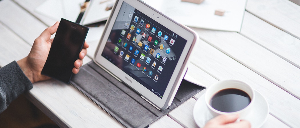 Een tablet in een hoes op een tafel tussen een smartphone en een kop koffie