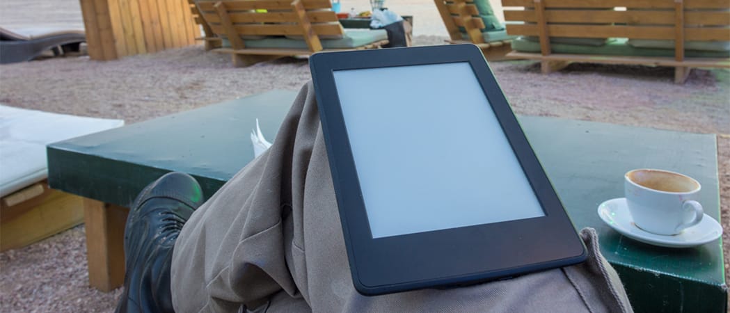 Man op het strand met een e-reader en een koffie.