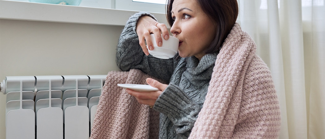 Een vrouw onder een elektrisch deken die koffie drinkt.